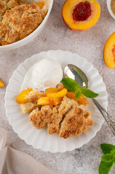 Homemade summer peach cobbler. Pie with juicy peaches, a scoop of vanilla ice cream and fresh mint on a white plate. Comfort food.