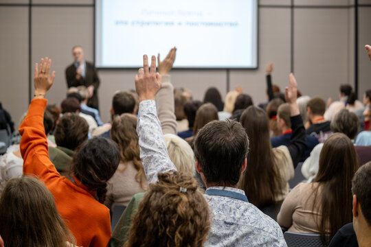 Audience at conference raising hands to ask questions during presentation, engaged participants in meeting room, interactive seminar atmosphere.