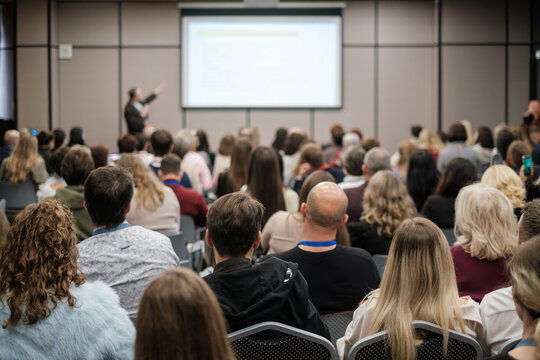 Crowd listening to business presentation, focused audience in modern conference room, professional meeting atmosphere, networking energy.