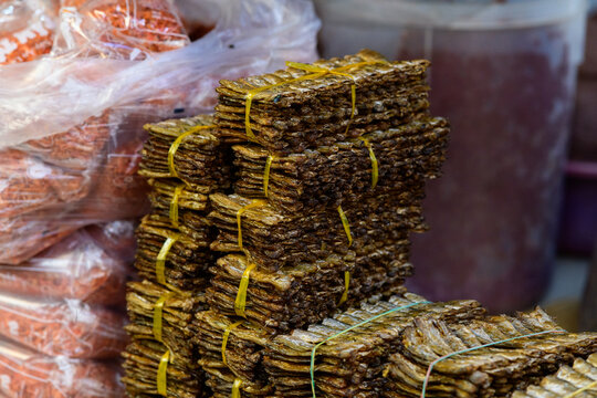 Neatly arranged bundles of dried fish tied with yellow plastic bands are stacked on a market counter in Kampot, Cambodia. The image highlights the textured surfaces and earthy tones of traditional