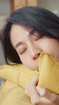 Vertical Screen : Young asian woman lay down on comfortable sofa in living room sleep after hard time work day and feel sick and bad, tired female fall asleep on couch at home, take nap or daydream.