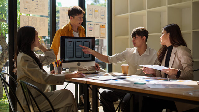 Collaborative UX UI design team reviewing mobile app wireframes and interface layouts on a modern workspace