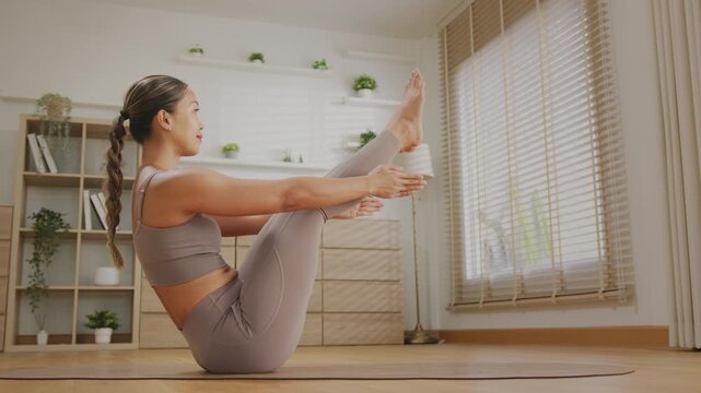 Asian Woman Practicing Yoga Meditation at Home in Morning Sunlight, Healthy Lifestyle Workout and Stretching on Fitness Mat, Calm and Focused Indoor Exercise in Minimal Living Room