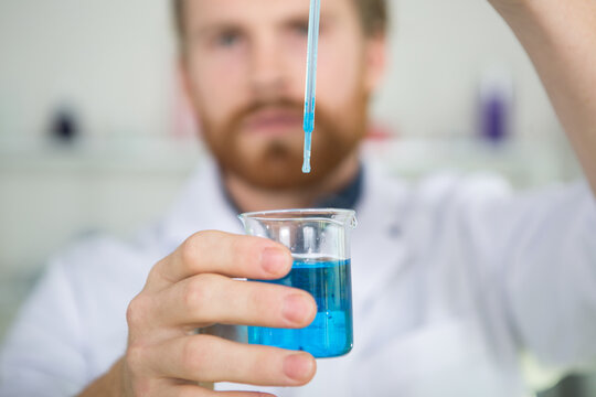 scientist dropping solution from pipette into flask