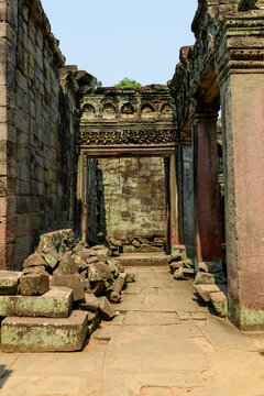 Ancient sandstone corridor with ornate lintel and scattered masonry inside Preah Khan temple, Angkor region, Cambodia. The textured stone surfaces and subtle moss evoke the monument's layered history