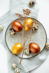 Golden and bronze Easter eggs in a gray plate on a linen napkin on a white background
