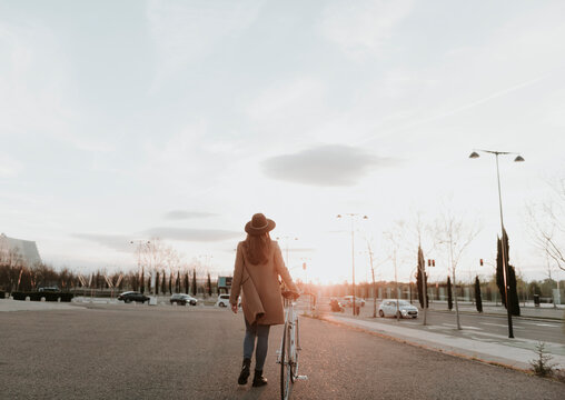 Young hipster woman going with a bicycle during sunset