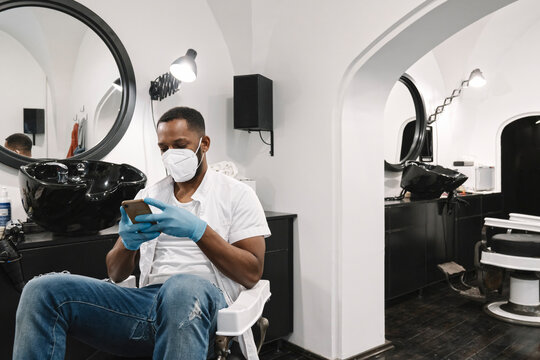 Barber wearing surgical mask and gloves using smartphone