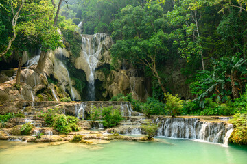 Soft daylight illuminates the multi-tiered limestone cascades and turquoise pools of Kuang Si Waterfalls, framed by dense tropical forest in northern Laos. Lush greenery and flowing water create a © Florent