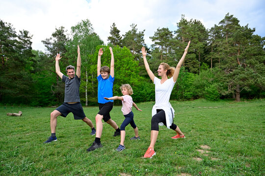 Family practicing warrior poses on grassy land in forest