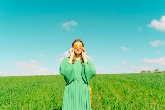 Blindfolded young woman wearing a green dress standing in a field