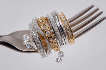Stacked diamond and gold wedding rings on a silver fork symbolizing love, engagement and celebration.
