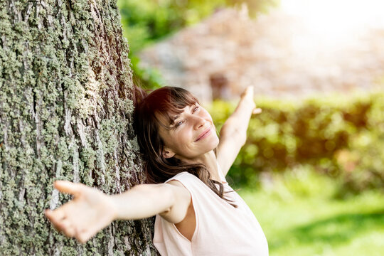 Portrait of smiling brunette woman leaning against a tree trunk
