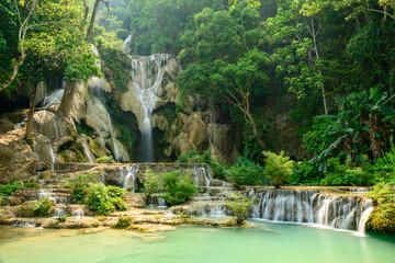 Soft sunlight highlights the terraced limestone cascades and turquoise pools of Kuang Si Waterfalls, surrounded by dense tropical forest in northern Laos. Lush greenery and flowing water create a © Florent