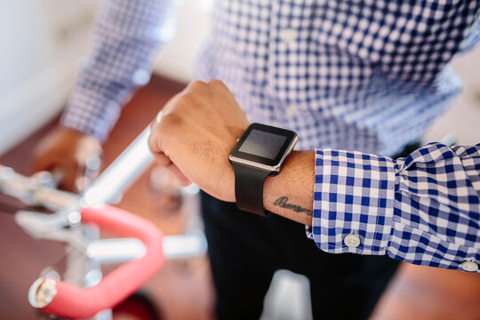 Close-up of man checking the smartwatch while holding a bike indoors