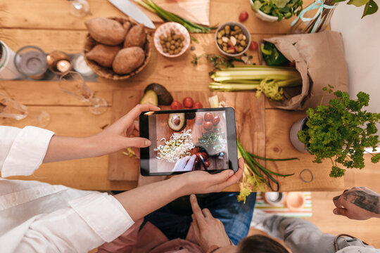 Friends cooking together taking picture of prepared vegetables with tablet, top view