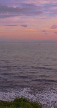 A serene vertical shot of a pink and purple sunset over the ocean with gentle waves crashing on the shore. Perfect for social media stories and mobile backgrounds.