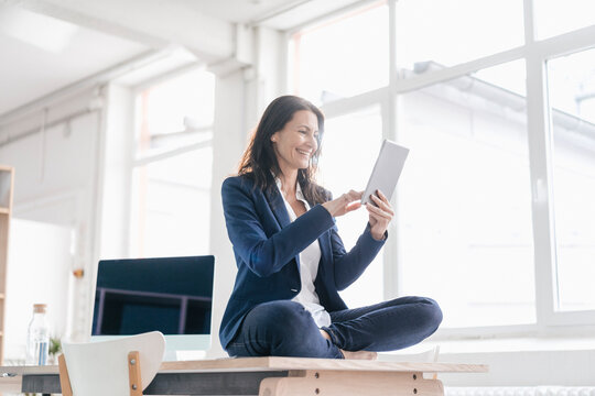 Businesswoman sitting on desk in a loft using tablet