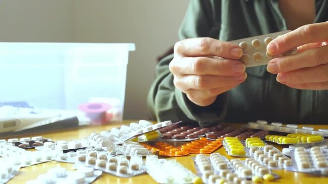 Close-up of female hands methodically arranging assorted tablets and capsules into neat piles on a wooden surface. Represents medication adherence strategy and chronic condition management routine.