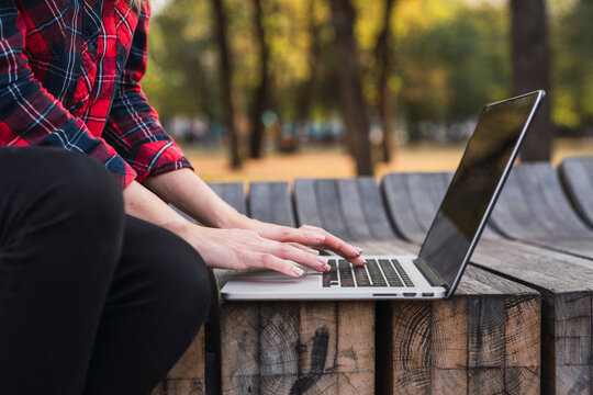 Young woman sitting on bench outdoors working on laptop, partial view