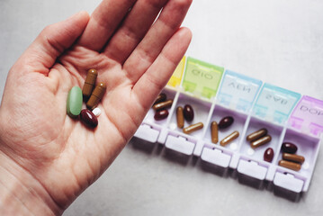 Female hand holding a handful of dietary supplements, close-up view. Weekly pill organiser.