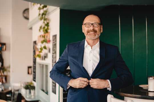 Confident mature businessman in a cafe buttoning his jacket