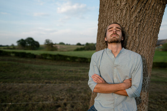 Relaxed young man leaning against a tree trunk in the countryside
