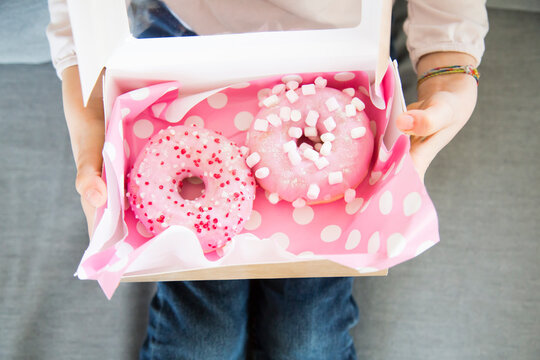 Girl holding box with doughnuts, partial view