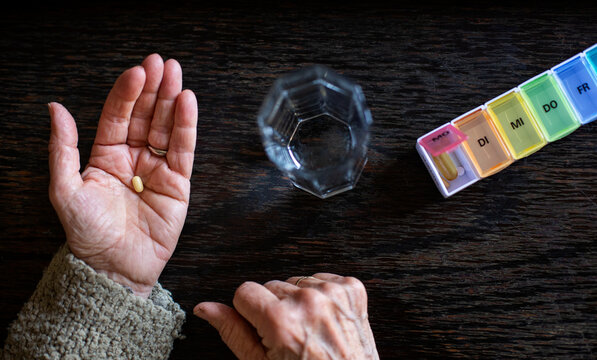 Senior woman taking medicine, water glass and pill organiser