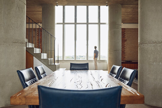 Wooden table in a loft flat with man at the window in background