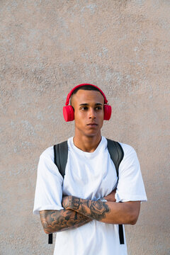 Portrait of tattooed young man listening music with wireless red headphones