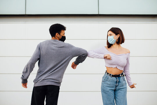Young couple wearing face mask greeting with elbow bump while standing against wall