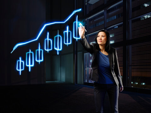 Asian businesswoman painting candle stick chart with light