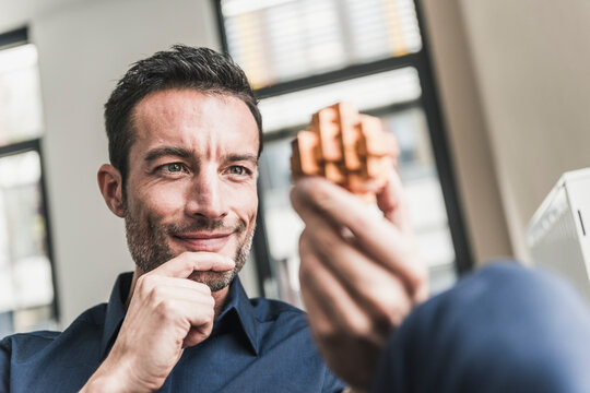 Mature man sitting in office assembling wooden cube puzzle