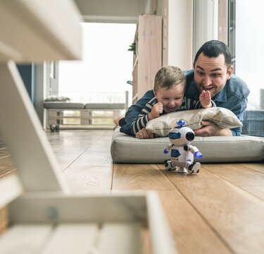 Excited father and son lying on a mattress at home watching a toy robot