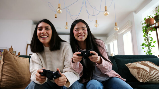 Diverse women enjoying multiplayer video game on sofa at home