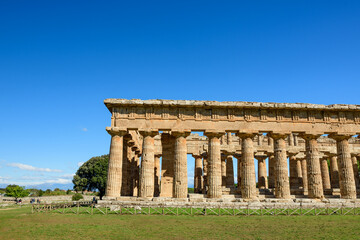 Fototapeta premium The imposing Doric columns of the Temple of Neptune stand in sharp relief against a clear blue sky at the archaeological site of Paestum, Italy. Sunlight casts crisp shadows on the weathered stone
