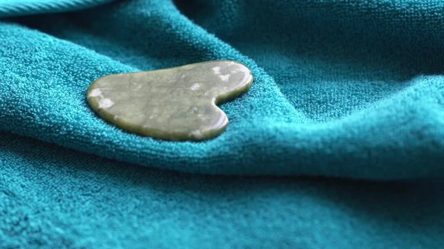 Guasha scraper made of natural serpentinite stone tool with soft towel, close-up