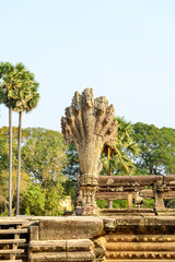 Obraz premium Close-up of a weathered sandstone naga balustrade at the entrance of Angkor Vat, Cambodia. The ancient serpent carving displays intricate textures and aged details, set against a clear blue sky and