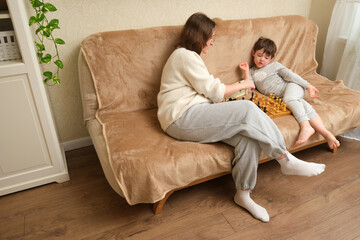 Obraz premium Woman and child playing chess on sofa. Family leisure activity at home. Intellectual game for brain development.