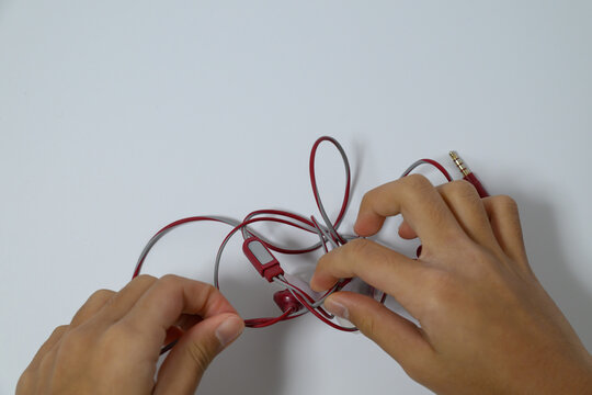 Close up of child hands untangling messy red earphone wires