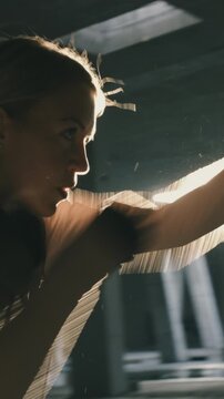 A focused athlete in a dimly lit gym, mid-exercise, showcasing determination and strength. Her intense expression and dynamic pose highlight dedication and effort in rigorous sport training.