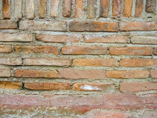 A wall of about 30 old brown bricks with jagged edges, held together with gray cement. The top...