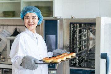 オーブンでパンを焼く衛生白衣を着た女性調理師　給食センター　給食室 © metamorworks