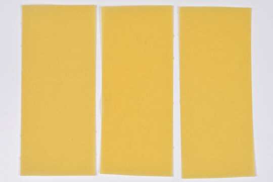 Three rectangular sheets of dry yellow lasagna pasta arranged side by side on a plain white background