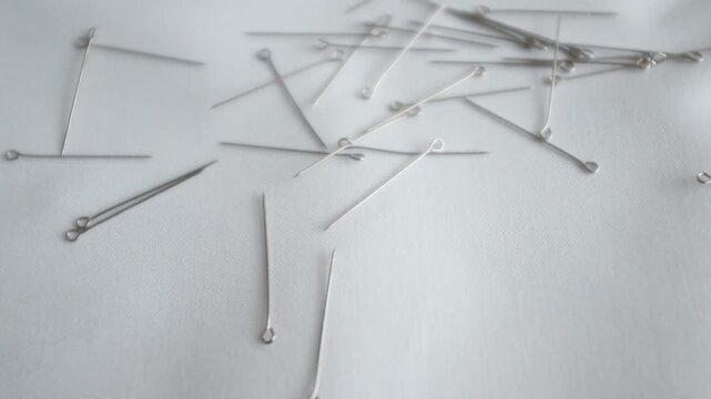 Professional-grade silver metallic sewing pins scattered on a clean surface. These fine-gauge steel dressmaker pins are for tailoring, delicate fabric draping, and high-fashion garment construction