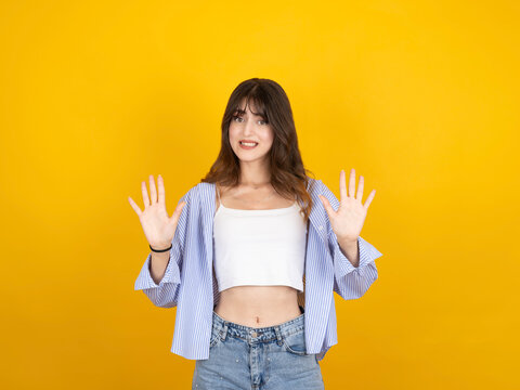 Concerned young woman showing stop gesture with both palms, looking at camera with hesitant expression against yellow background. Concept of rejection, social distancing, denial, and saying no.