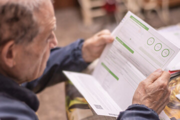 An elderly man studies an electricity bill. Pension. Electricity costs and payments of an elderly household. Financial problems and worries. © Tatiana