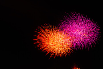 右側にあるオレンジ色とピンク色の夜に光り輝く複数の花火
