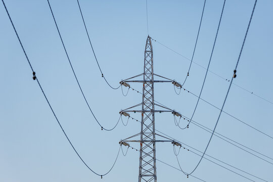 High-voltage lattice transmission tower supporting multiple levels of power lines stretching in catenary curves across clear blue sky.